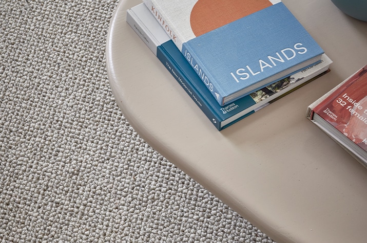 This image features the Urban Instinct Kensington Grove Wool Carpet in Pebbled Oyster, creating a refined and comfortable setting. The Pebbled Oyster colour provides a neutral yet sophisticated backdrop, perfectly complementing the modern decor elements. The texture of the wool carpet adds a layer of warmth and luxury, making it ideal for living rooms and other high-traffic areas. The scene, with books and a stylish vase on a table, emphasizes the carpet's role in enhancing both the aesthetics and comfort of the room. This wool carpet from the Kensington Grove collection is designed to offer both beauty and durability.