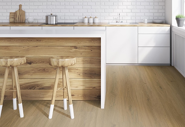 This image showcases Aspecta XL-Plank Macadamia Hybrid flooring in a sleek, modern kitchen. The Macadamia colour offers warm, natural wood tones, enhancing the bright and minimalistic design of the space. The wide planks create a clean and expansive look, while the wood grain adds a touch of natural elegance. The combination of the white cabinetry and natural wood accents gives the kitchen a cosy, yet contemporary feel. This Hybrid flooring provides both durability and style, making it an ideal choice for high-traffic areas such as kitchens and dining spaces.
